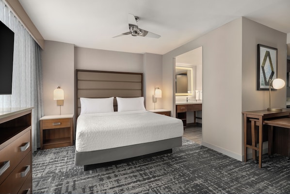 Habitación de hotel con una cama grande, mesitas de noche, un escritorio, un espejo y un ventilador de techo.