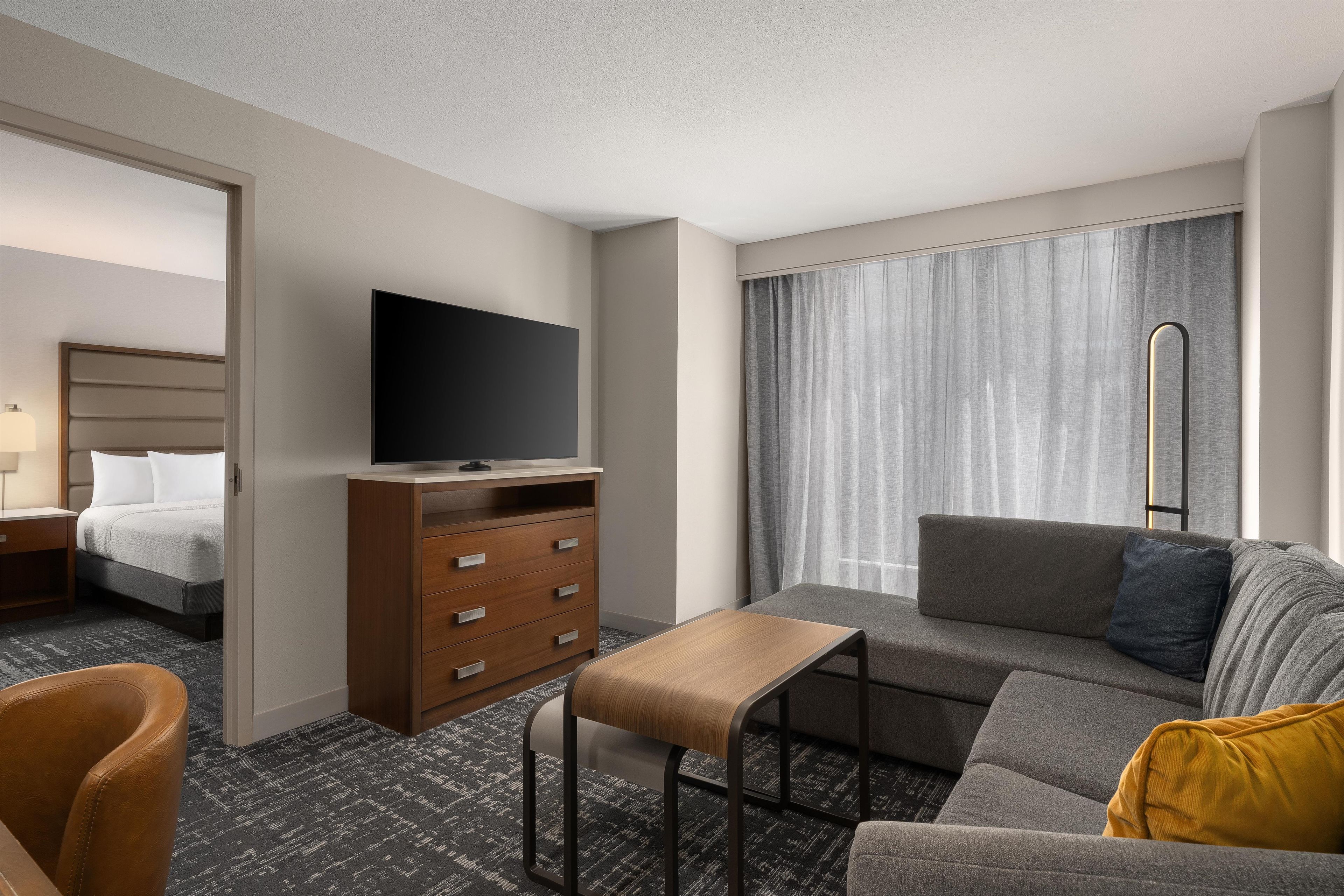 A hotel room with a bed, a TV, a sofa, a desk, and a window with curtains.