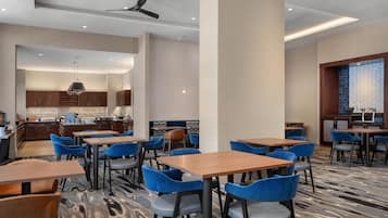Uma sala de jantar moderna com mesas e cadeiras, uma cozinha ao fundo e um ventilador de teto.