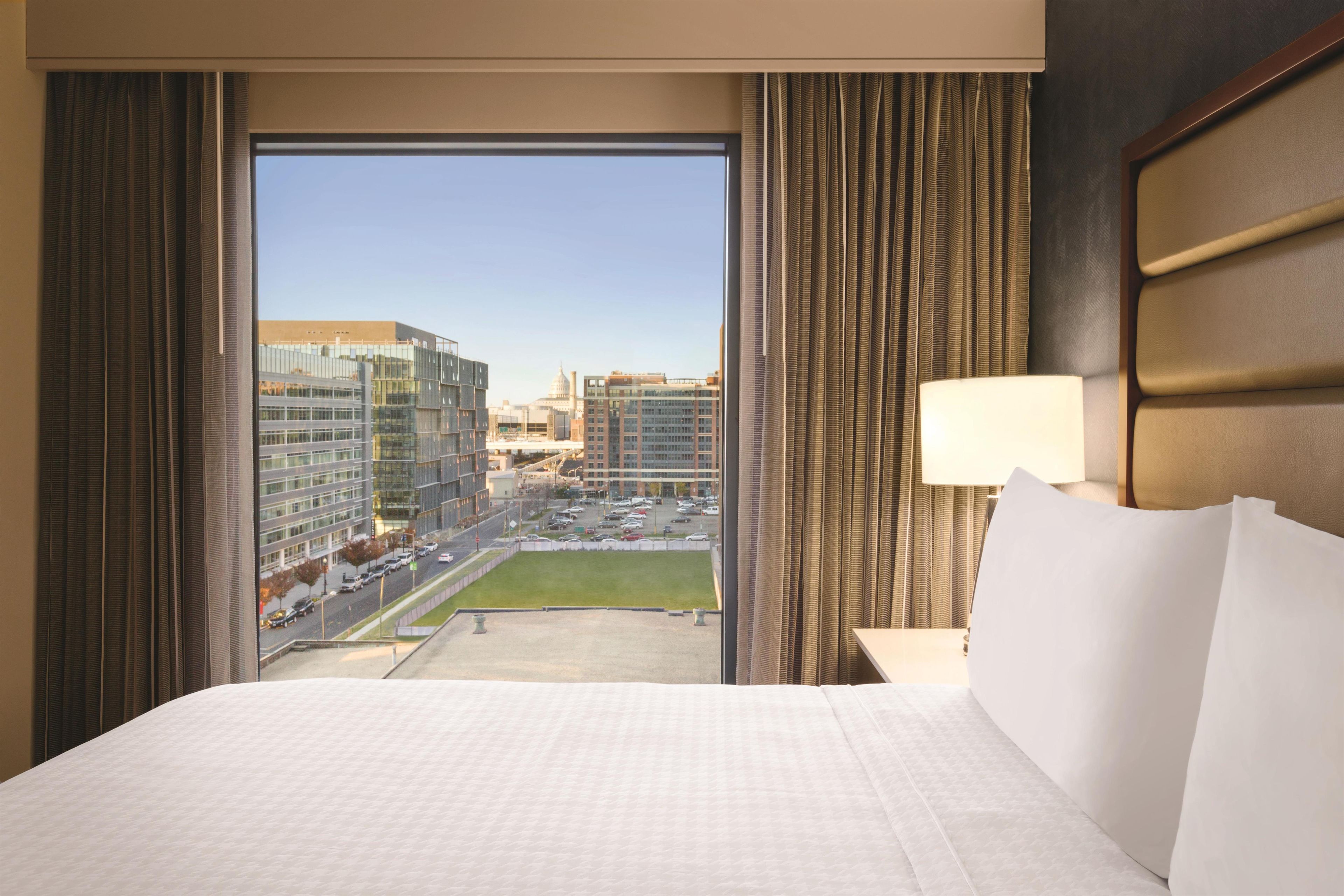 A hotel room with a large bed, a view of a cityscape, and a window with curtains.