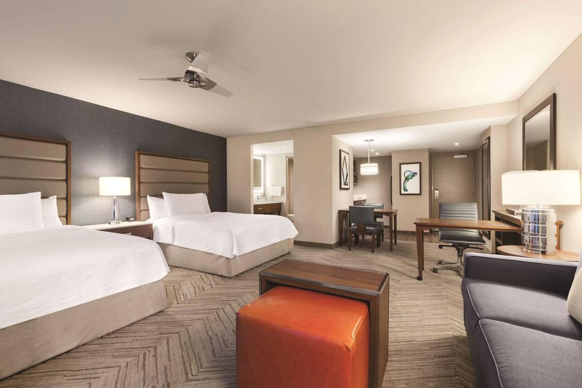 Une chambre d’hôtel avec deux lits, un bureau, une chaise, un canapé, une table basse, un ventilateur de plafond et un miroir.