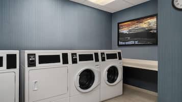 A laundry room with two front-loading washers and dryers, a clock on the wall, and a painting above the dryers.