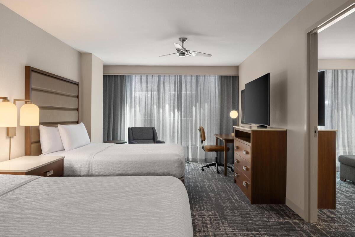 Habitación de hotel con dos camas, un escritorio, una silla, un televisor y un ventilador de techo.