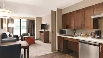 Une chambre d’hôtel équipée d’une kitchenette, d’un coin repas avec une table et des chaises, d’un canapé, d’une télévision et d’une grande fenêtre avec des rideaux.