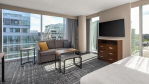 Ein modernes Hotelzimmer mit großem Fenster, einer Couch, einem kleinen Tisch, einem Fernseher und einem Bett.