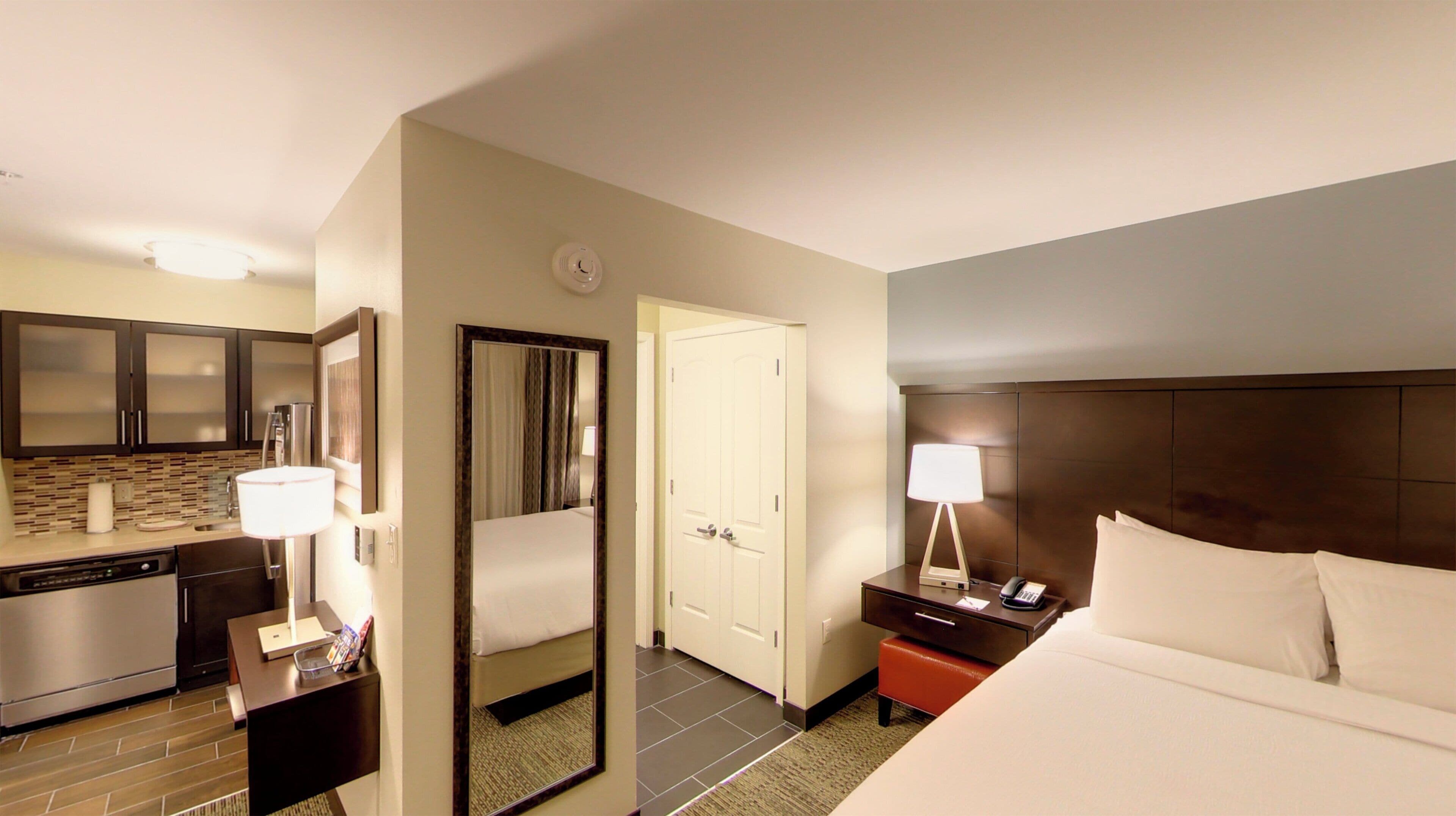Una habitación de hotel con cama, mesita de noche, lámpara y espejo.