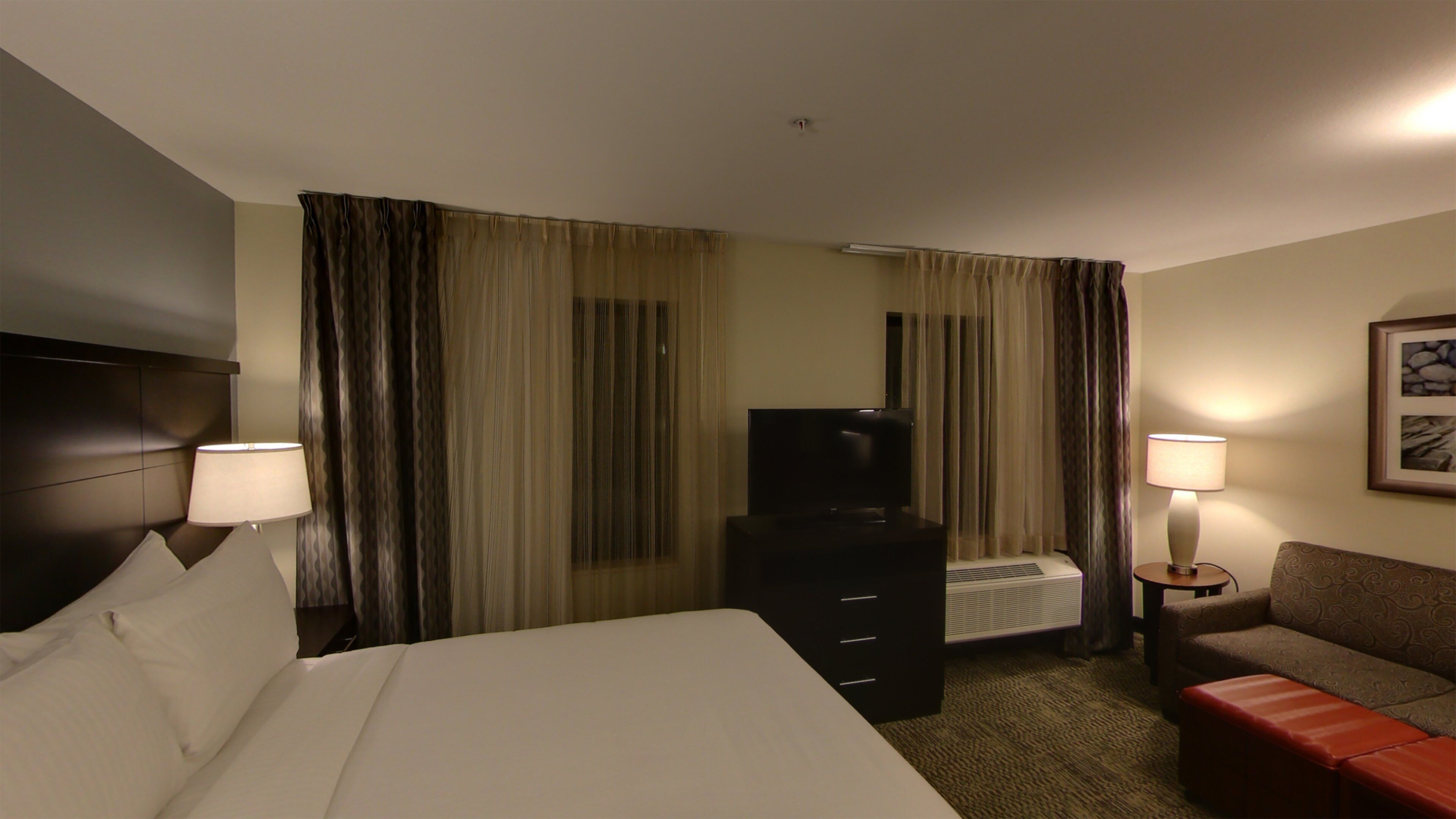 A hotel room with a bed, a TV, a desk, a chair, and two lamps.