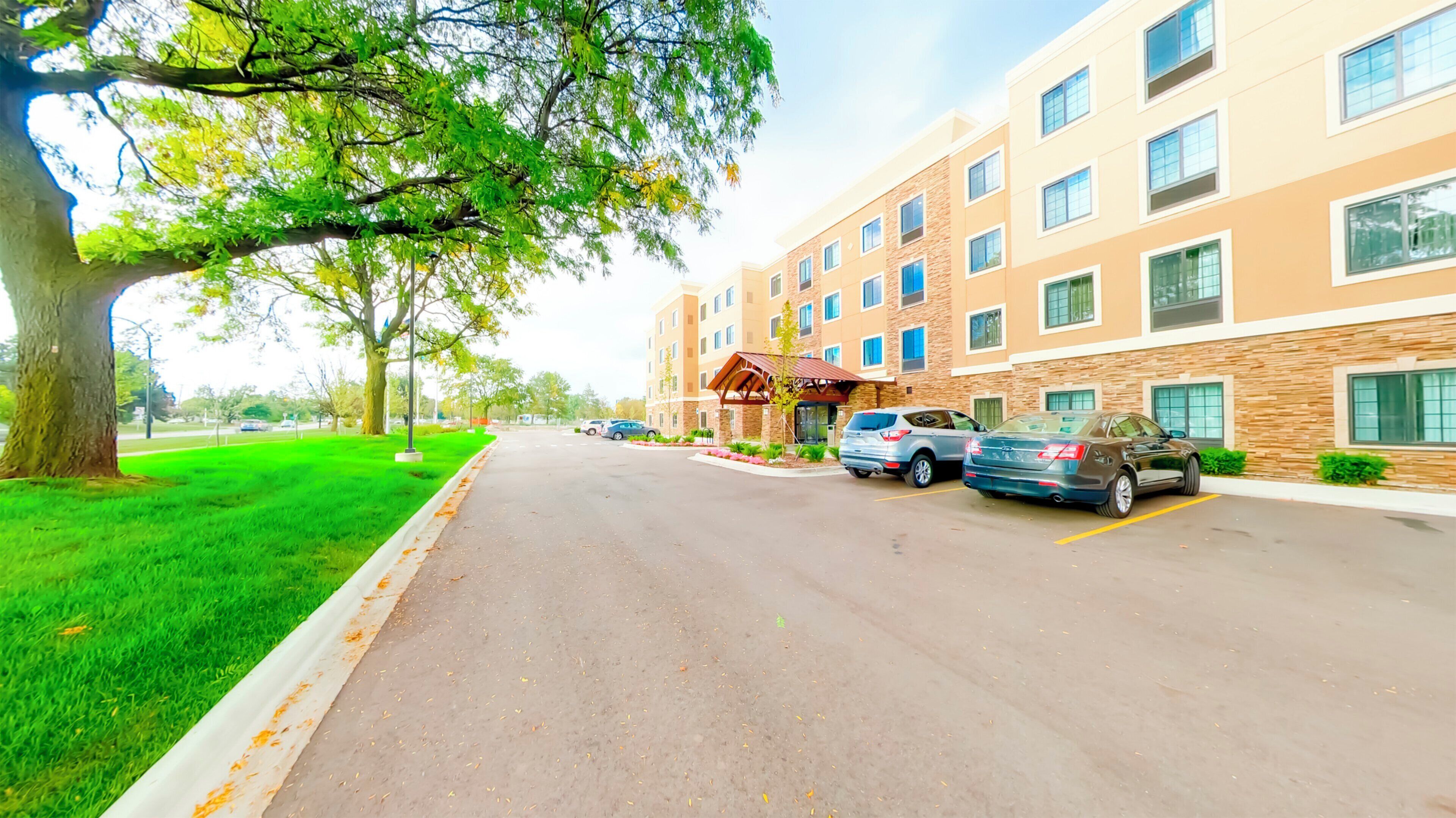 A multi-story hotel with a parking lot, a covered entrance, and a well-maintained lawn.