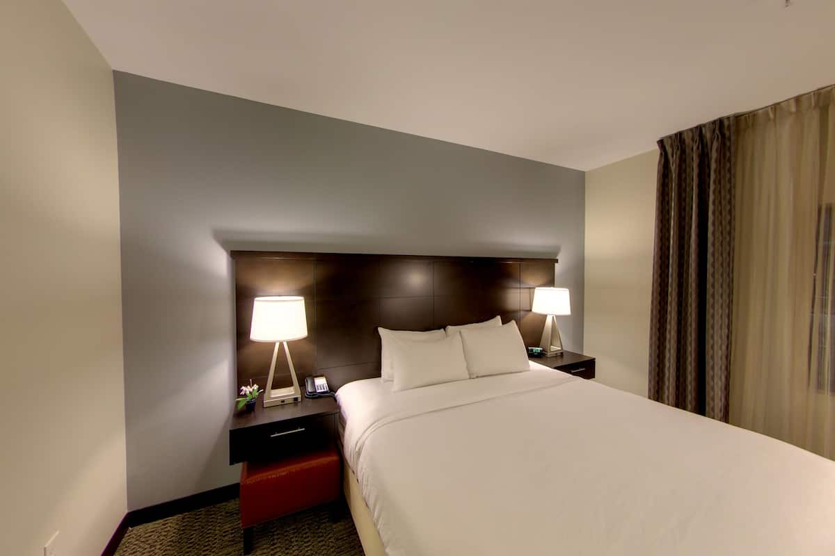 Une chambre d’hôtel avec un grand lit, deux tables de chevet avec des lampes, un banc rouge et une tête de lit sombre.