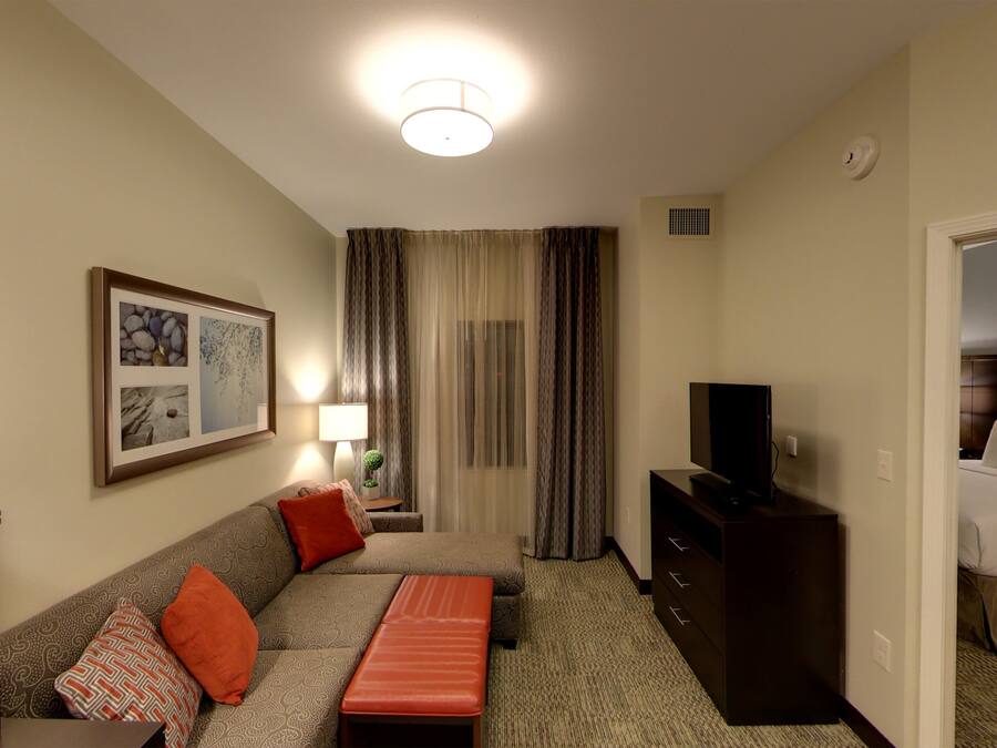 A hotel room with a sofa, a small table with a lamp, a television on a stand, a bed, and a framed picture on the wall.