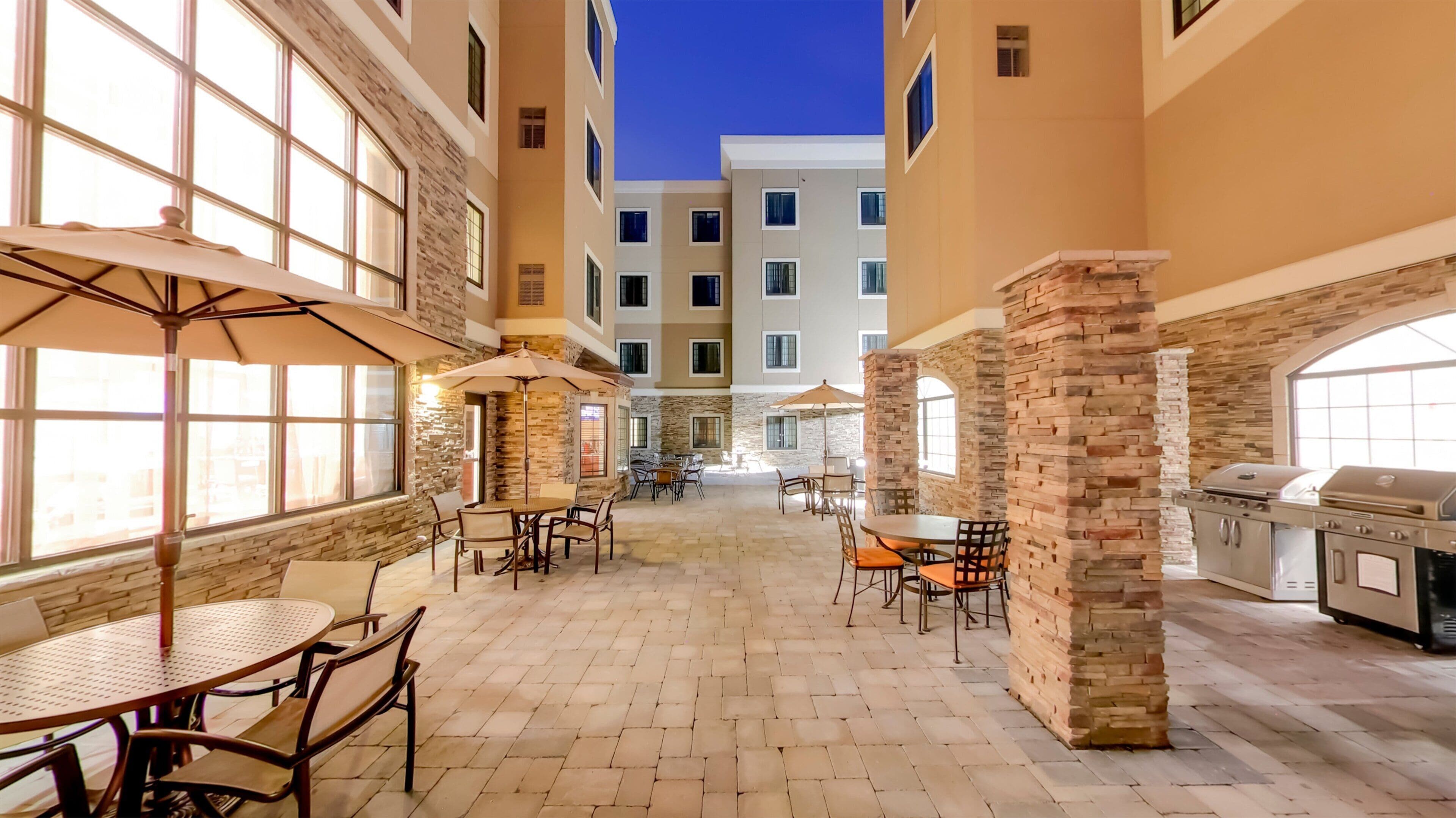 An outdoor patio area with tables and chairs, stone pillars, and a barbecue grill.