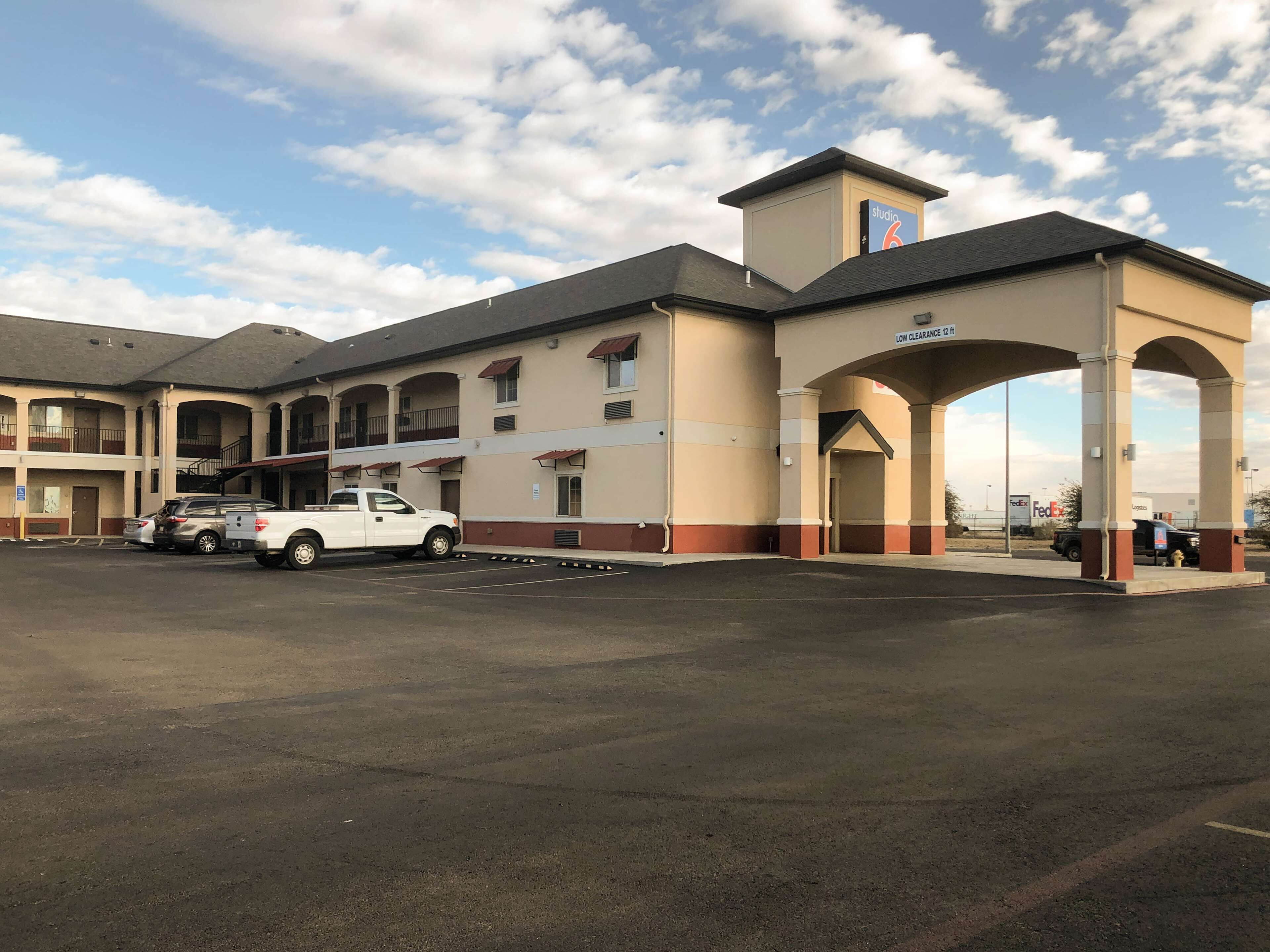 A motel with a central entrance, multiple balconies, and a parking area with several vehicles.