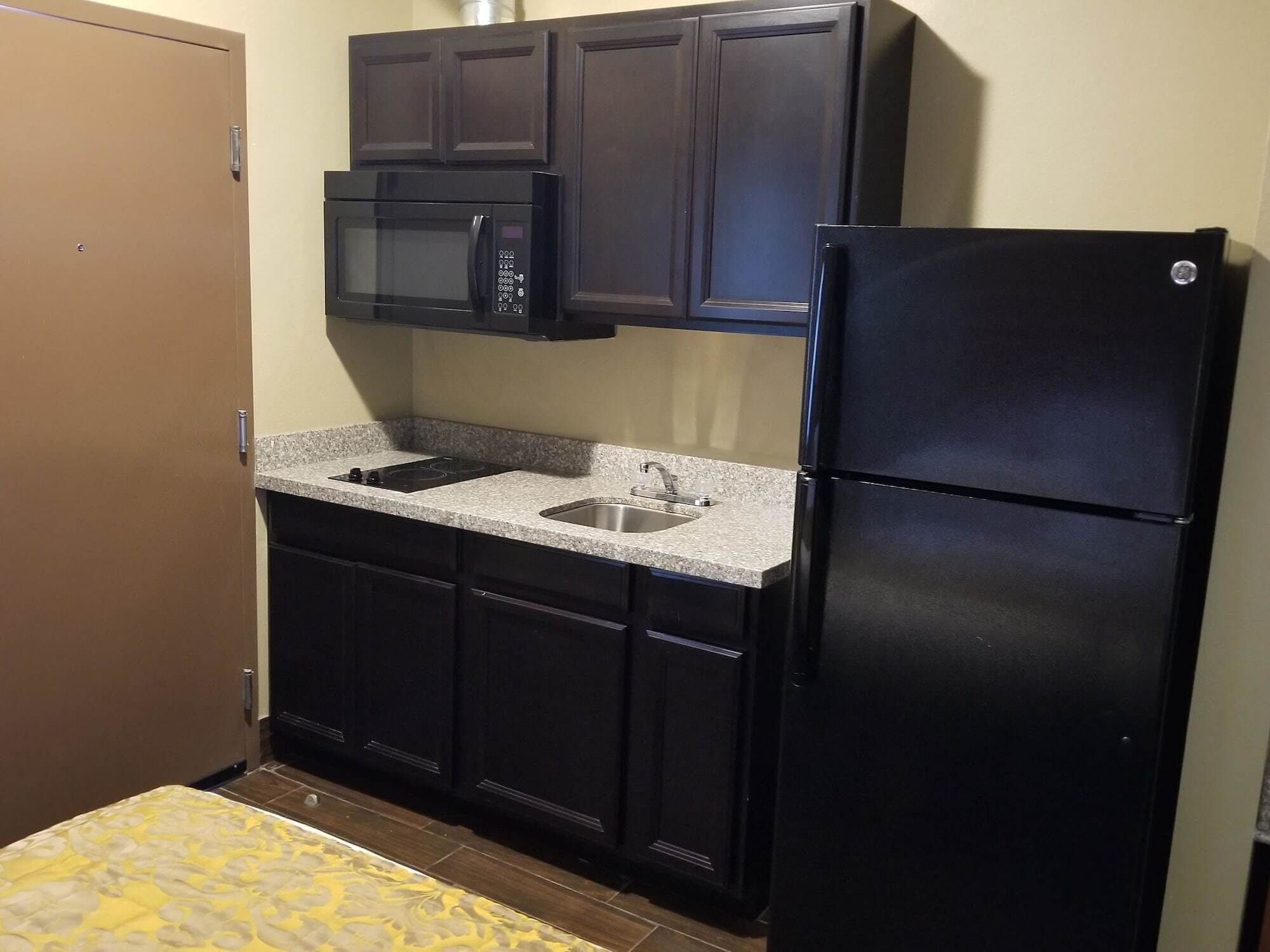 A compact kitchen with dark cabinets, a black refrigerator, a microwave, and a sink.