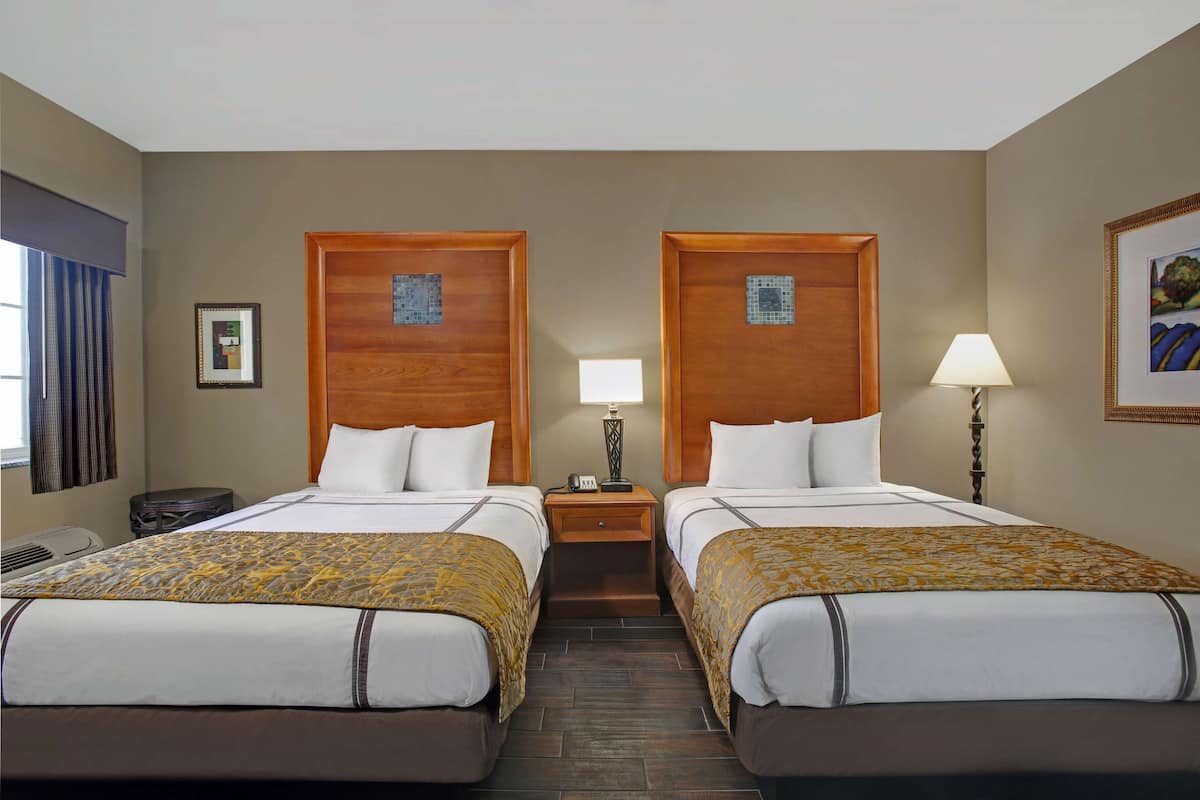 A hotel room with two beds, a nightstand with a lamp, a framed picture on the wall, and a window with curtains.