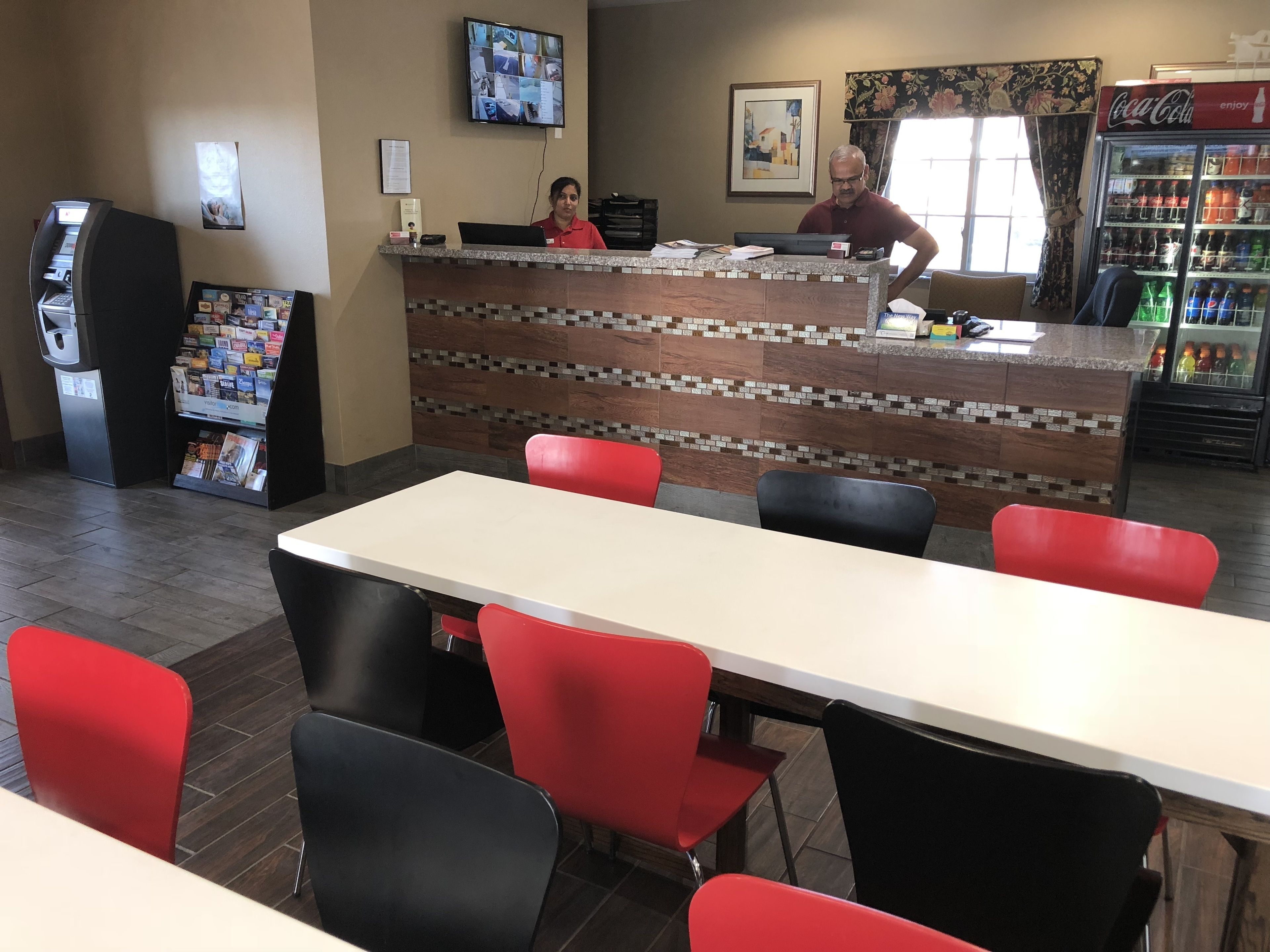 Un restaurant avec un comptoir, des chaises rouges et noires, un réfrigérateur Coca-Cola et un écran numérique au mur.