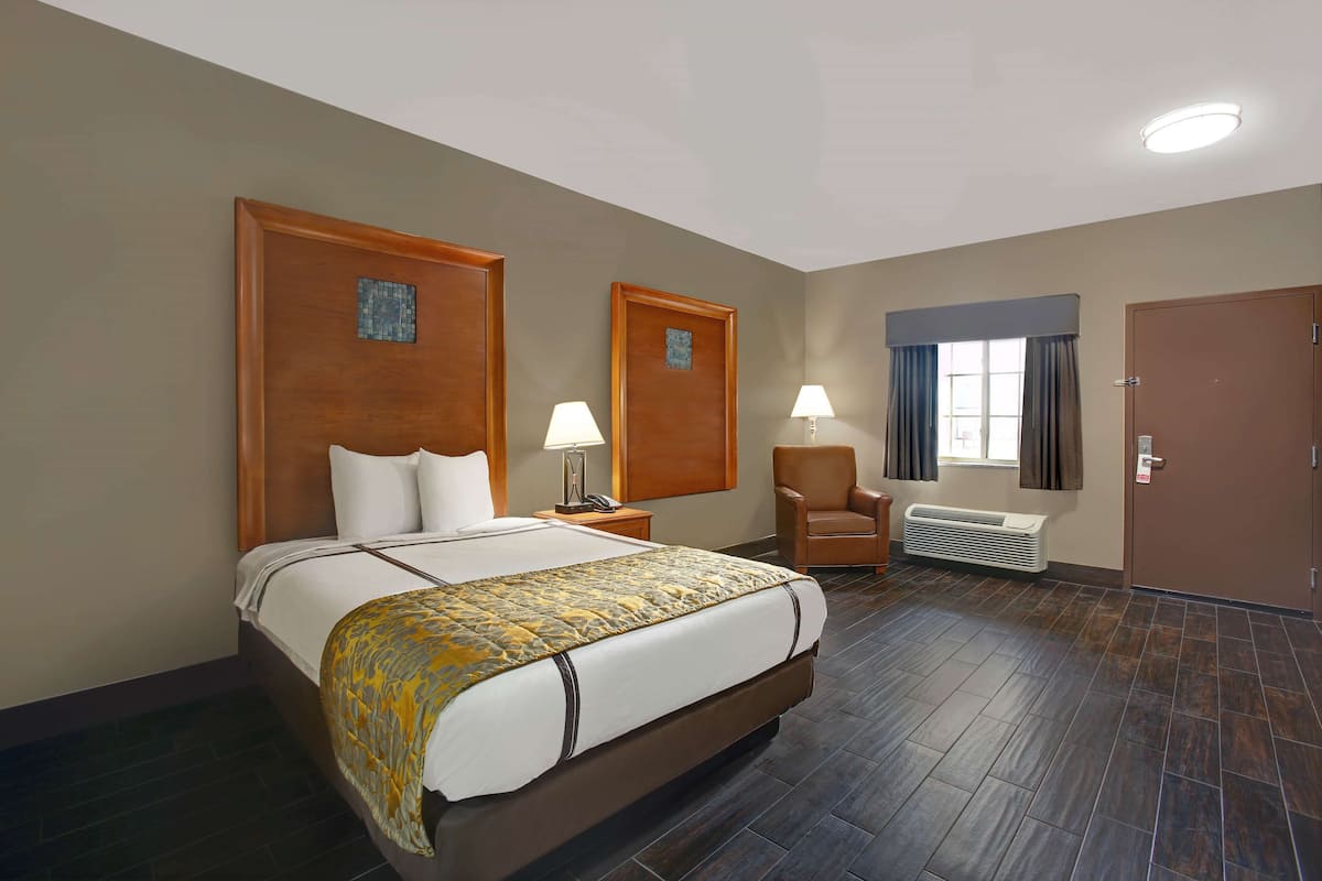 A hotel room with a large bed, two bedside tables, a chair, a window with curtains, and a door.