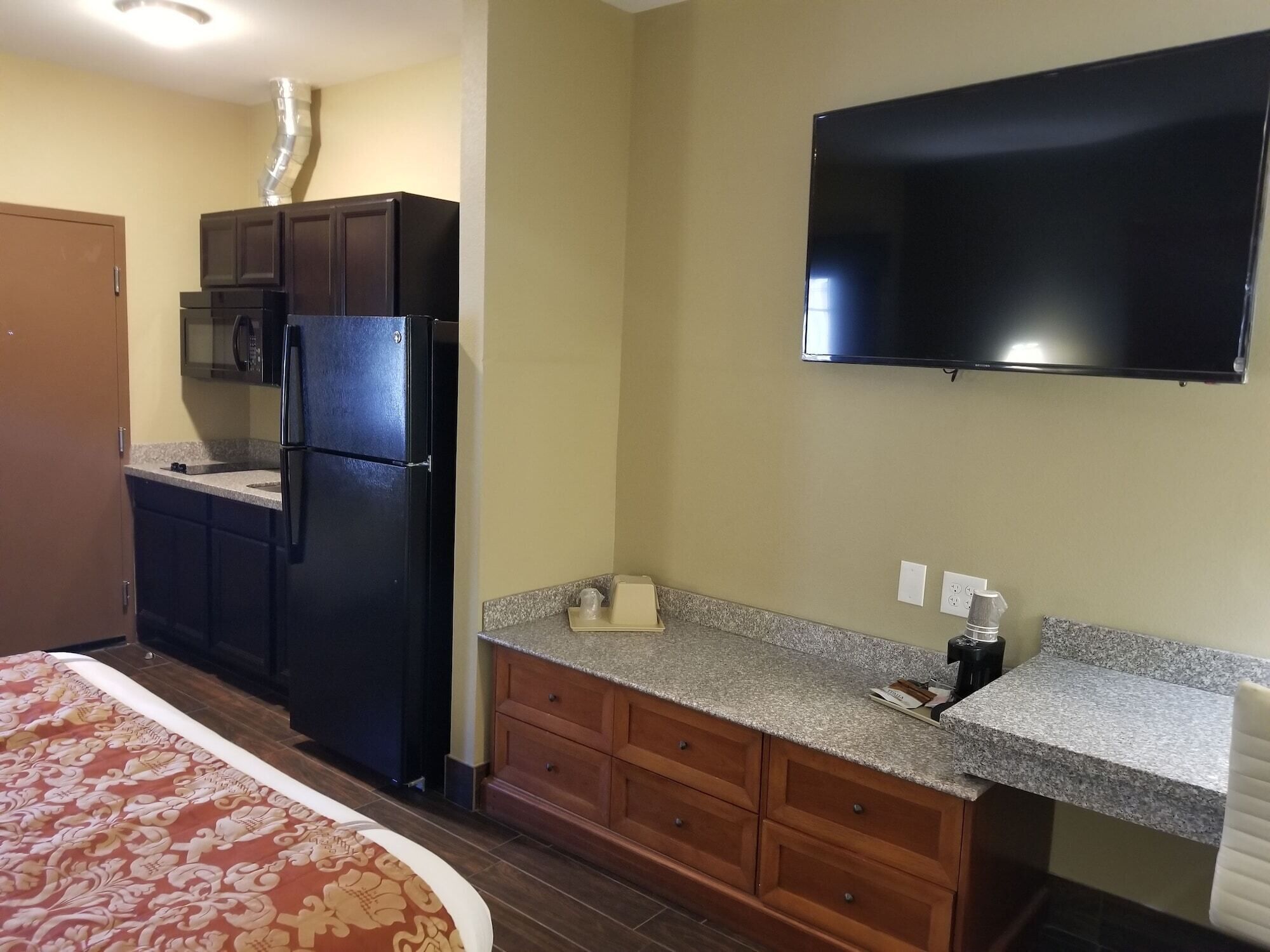 Una cocina compacta con refrigerador, microondas y un televisor de pantalla plana montado en la pared.