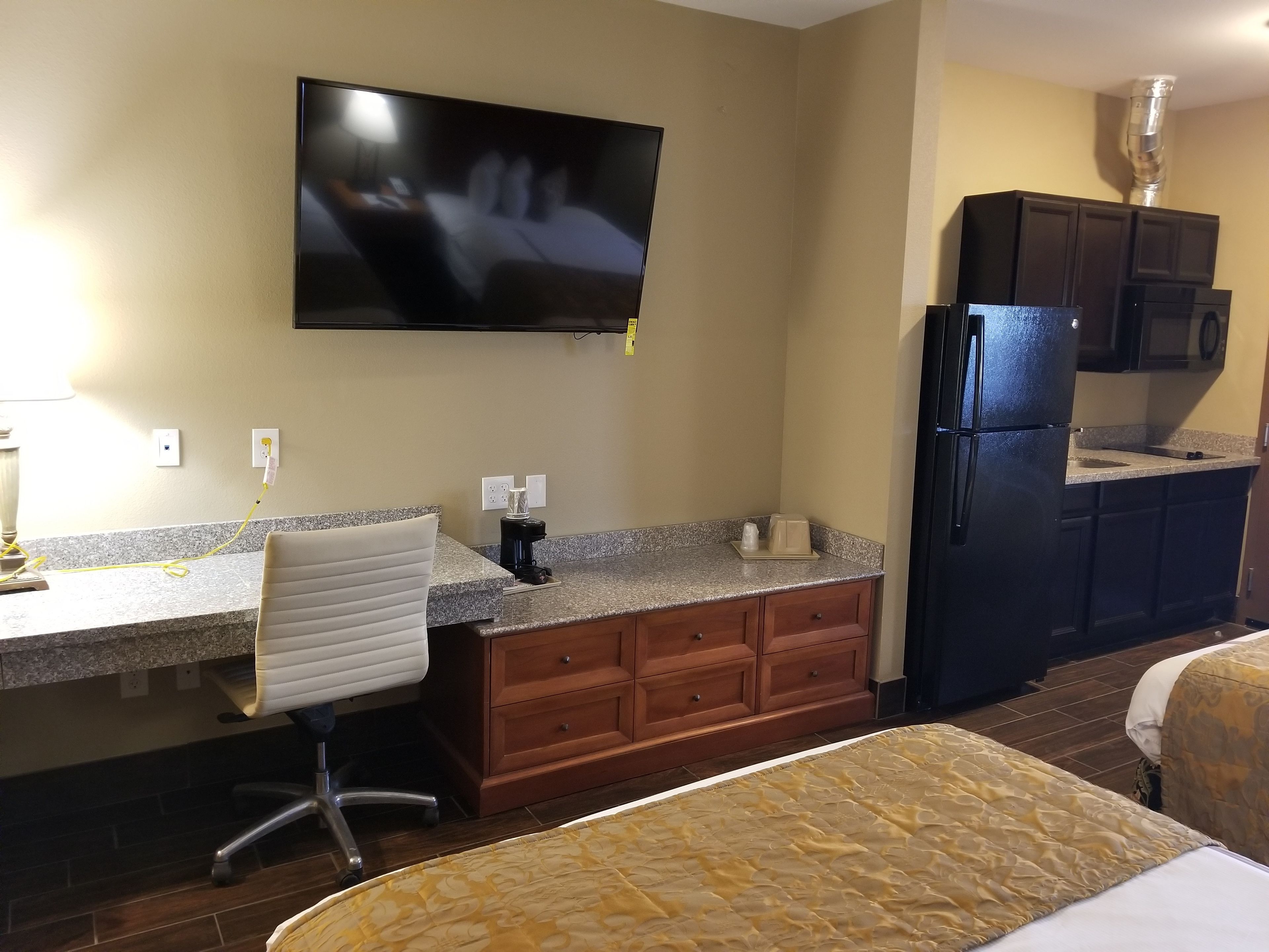 A hotel room with a bed, a desk with a chair, a television mounted on the wall, a refrigerator, and a microwave.