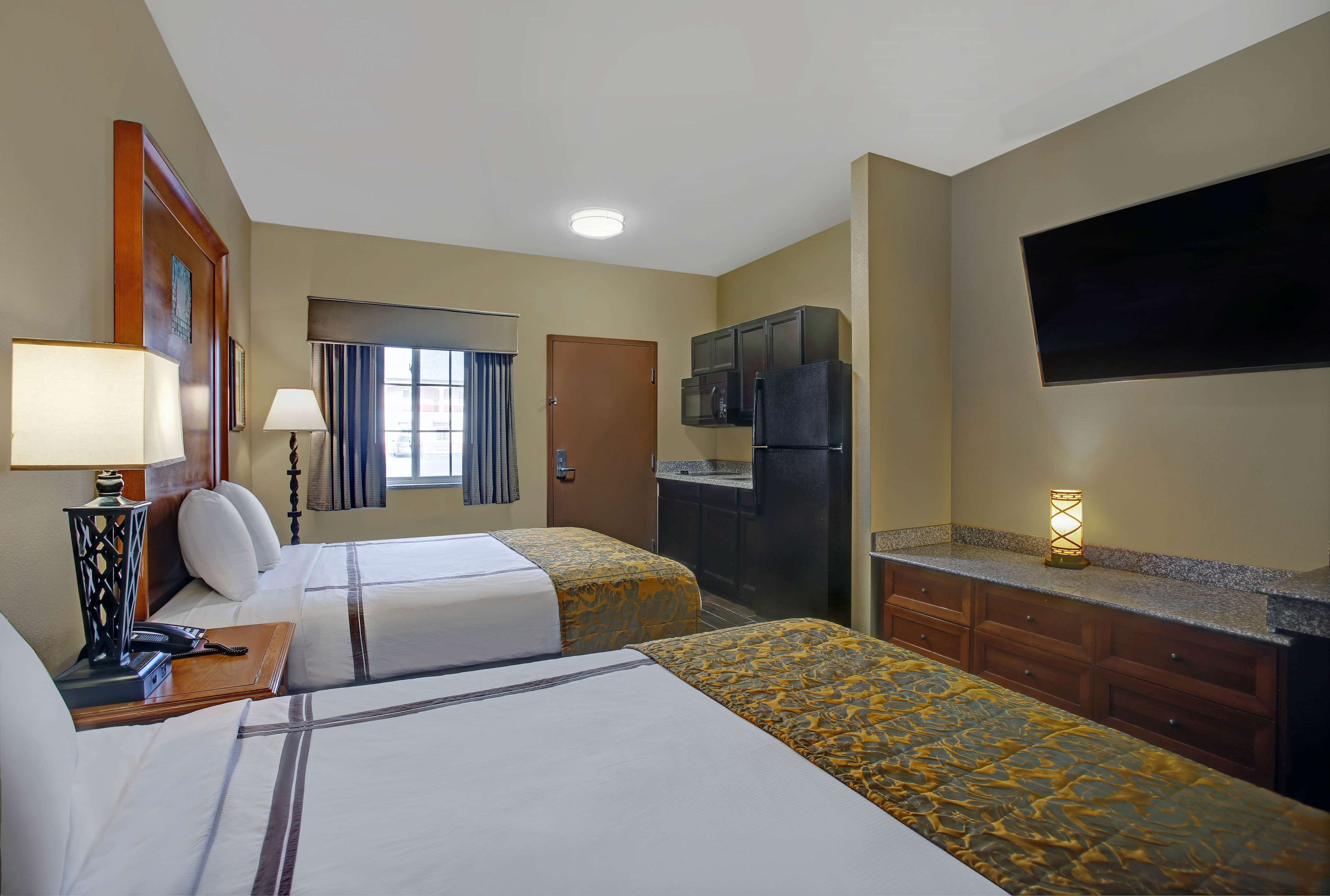 Une chambre d’hôtel avec deux lits, un bureau avec une lampe, un téléviseur à écran plat, un minibar et une porte donnant accès à la salle de bain.