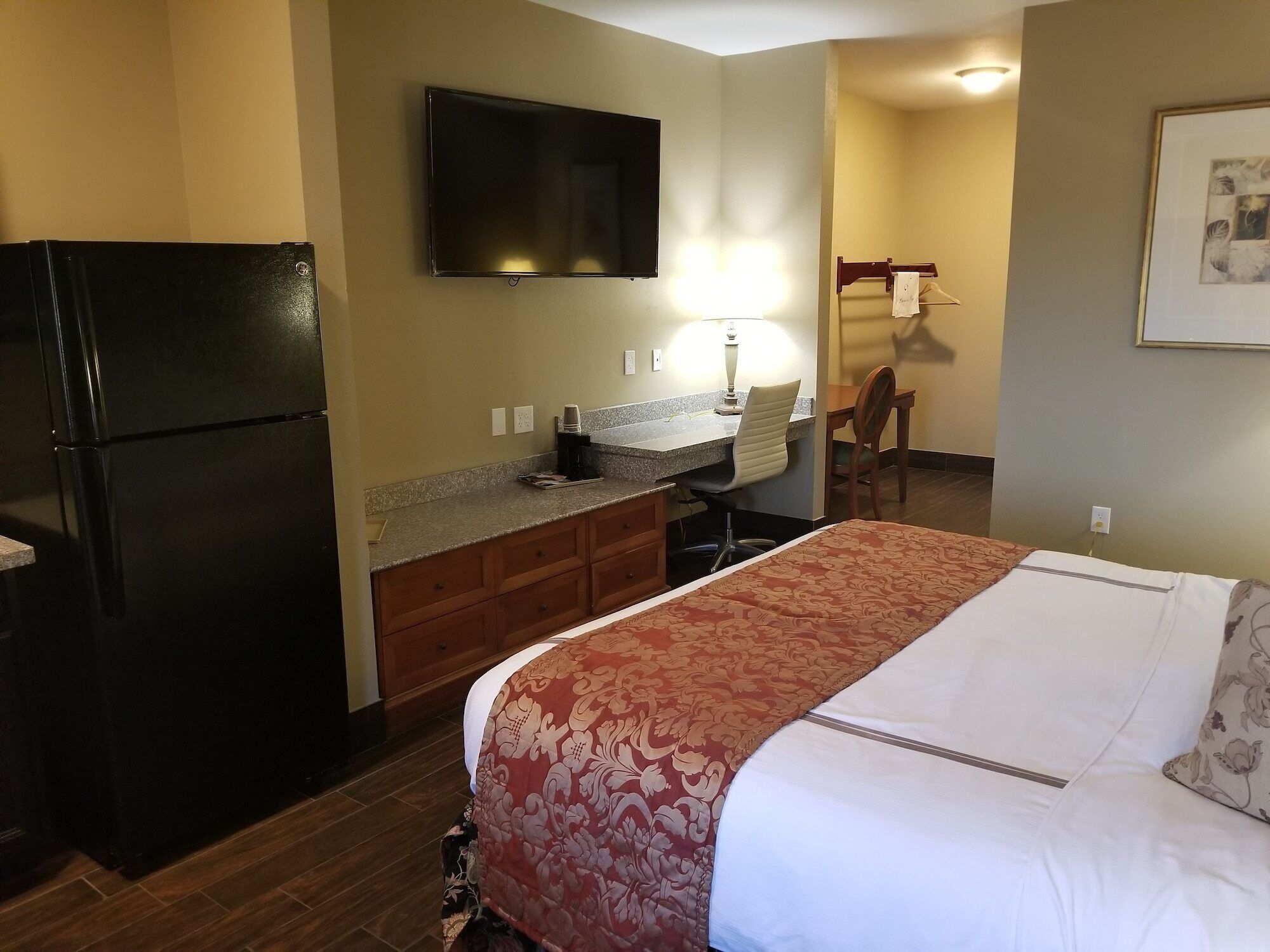 A compact hotel room with a bed, a kitchenette, a TV, and a desk.