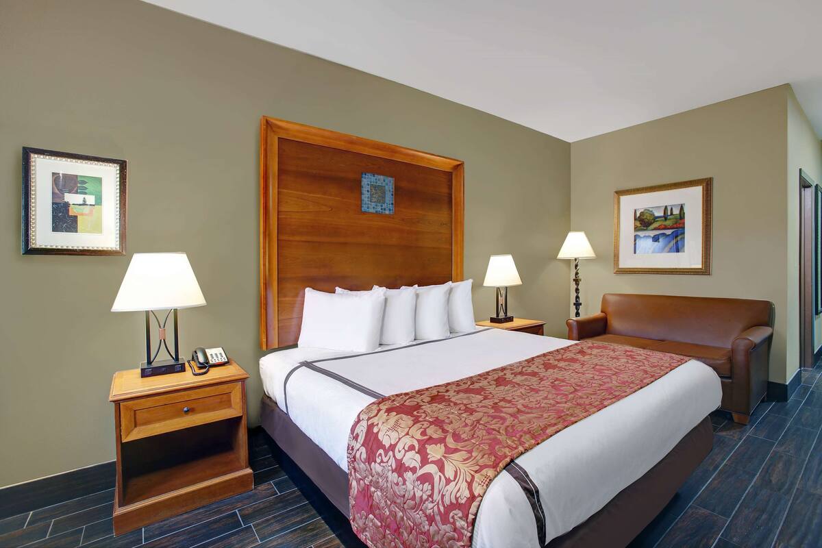 A hotel room with a large bed, two bedside tables with lamps, a wooden headboard, and artwork on the walls.