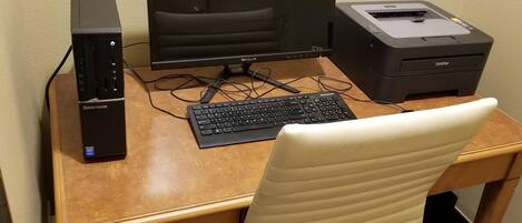 A wooden desk with a black monitor, a black keyboard, a printer, and a laptop.