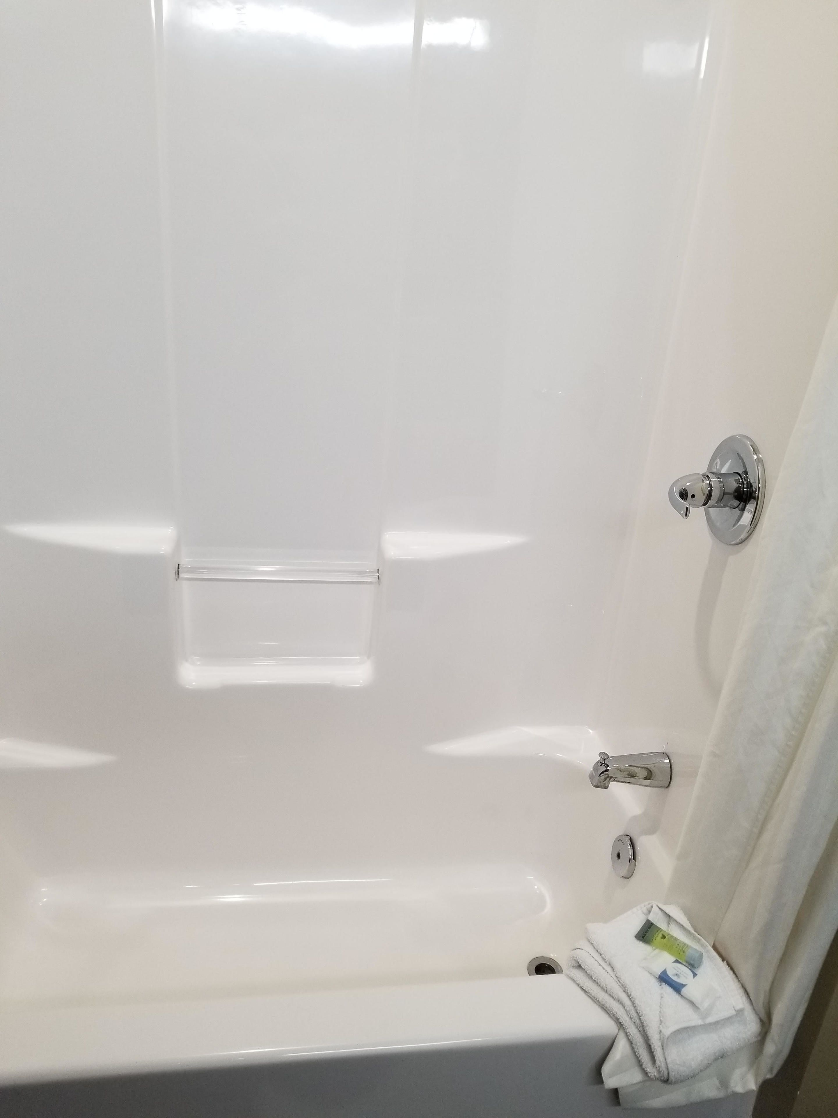 A white bathtub with a chrome faucet, a clear glass shelf, and a towel hanging on the wall.