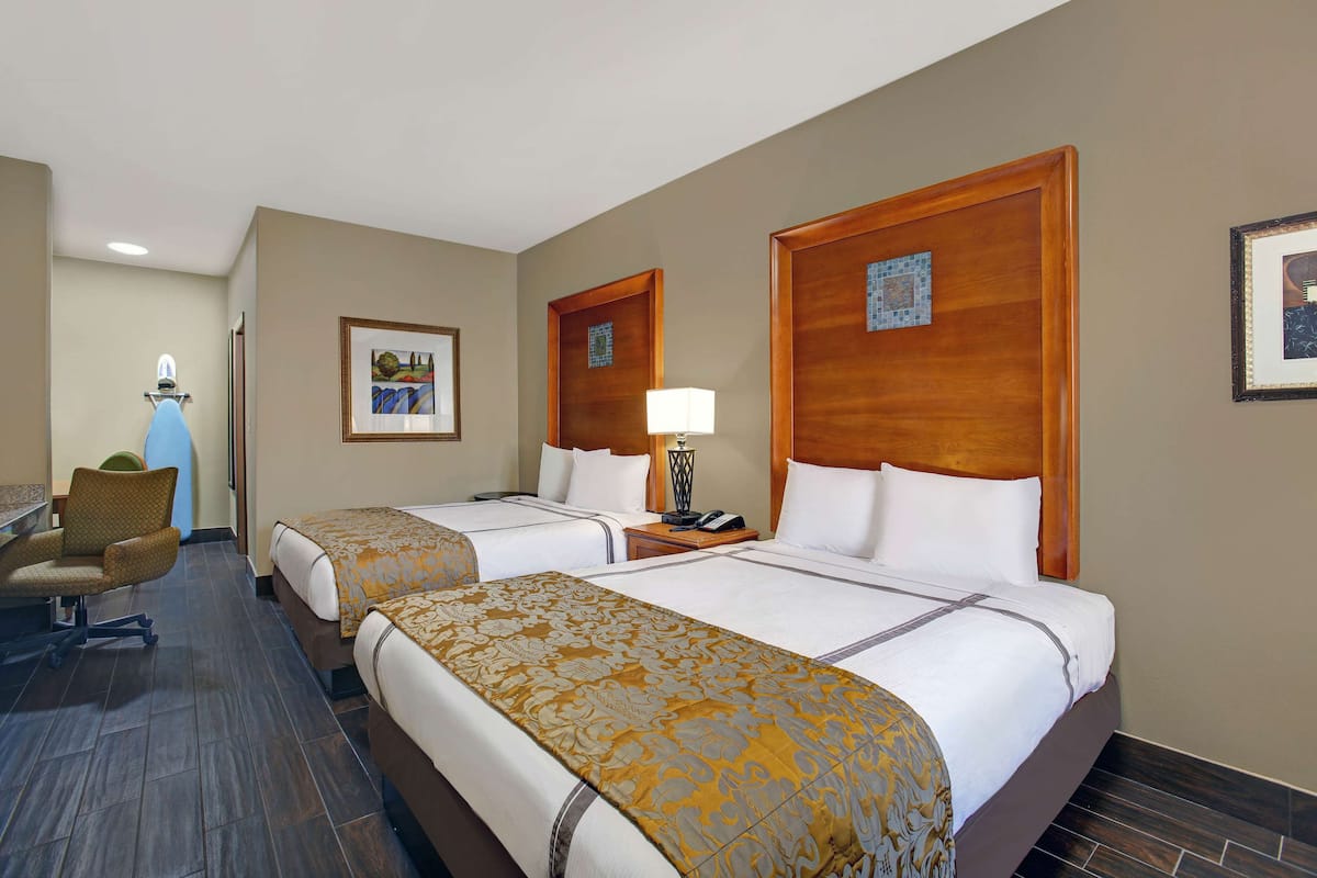 A hotel room with two beds, a desk, and a chair.