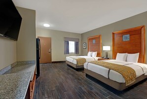 Habitación de hotel con dos camas, un televisor, una puerta y un ventanal con cortinas.