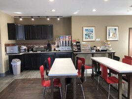 Una cocina moderna con armarios oscuros, encimera blanca y una zona de café. Hay sillas rojas alrededor de una mesa central.