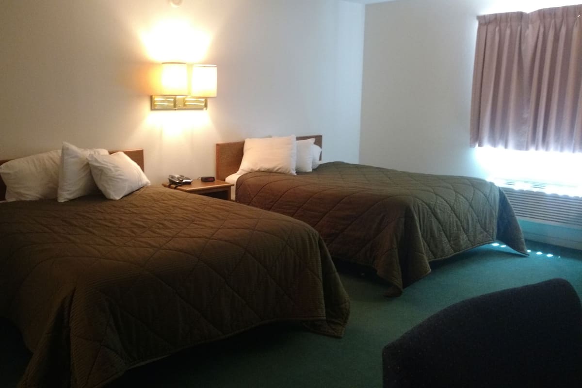Een hotelkamer met twee bedden, een nachtkastje, een lamp en een raam met gordijnen.