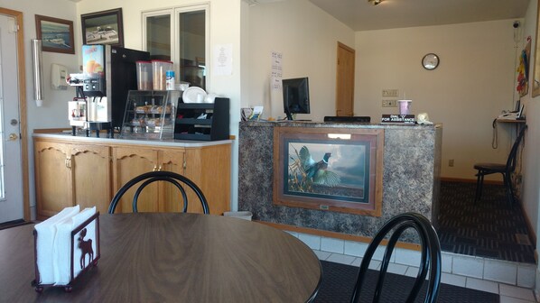 A reception area with a counter, a coffee machine, a refrigerator, a framed picture, and a clock on the wall. - Dakota HorizINN (Parkston)