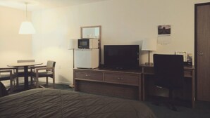 Ett hotellrum med en säng, ett skrivbord med en tv, en mikrovågsugn och en stol.