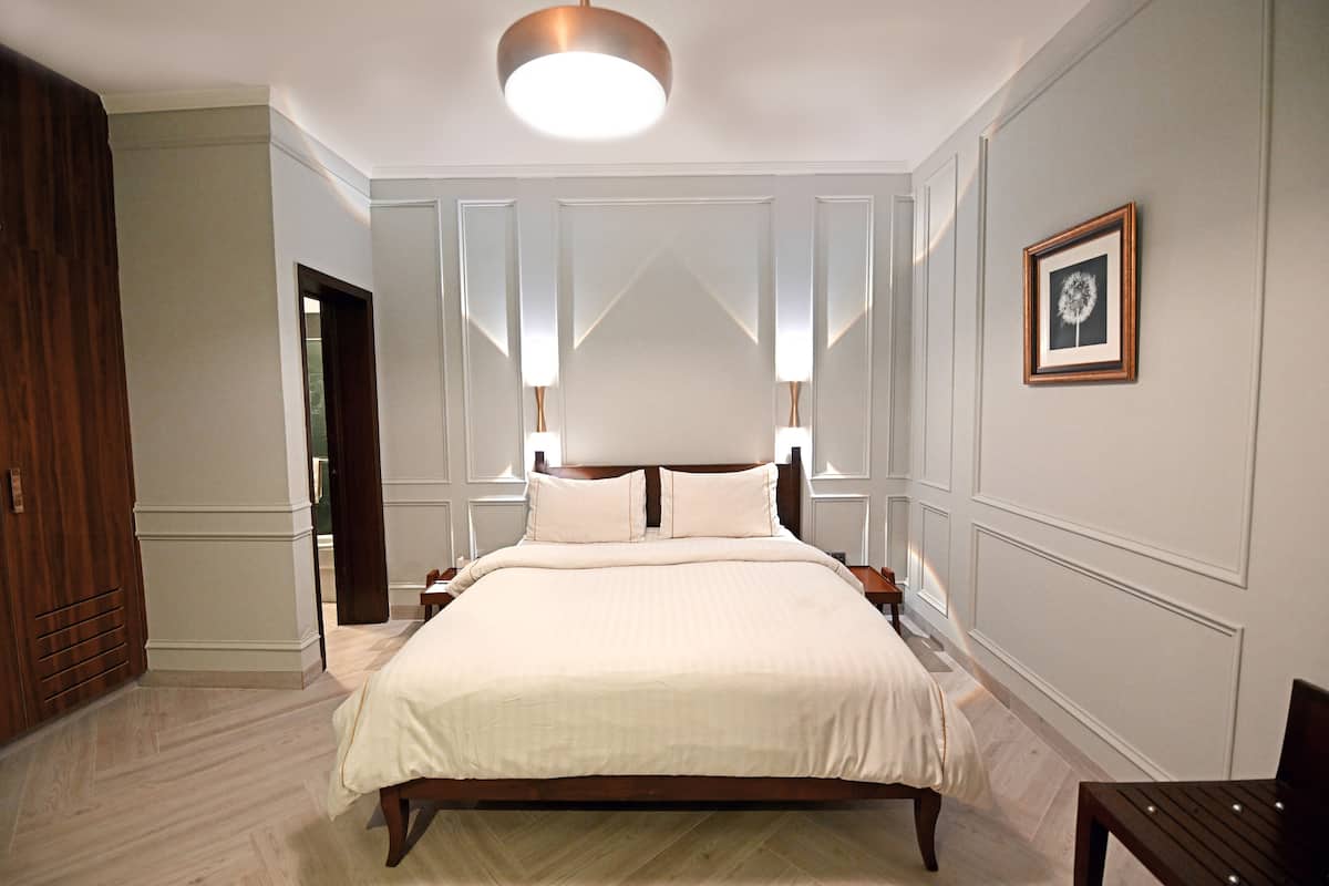 A spacious bedroom with a large bed, wooden headboard, bedside tables, and a framed picture on the wall.