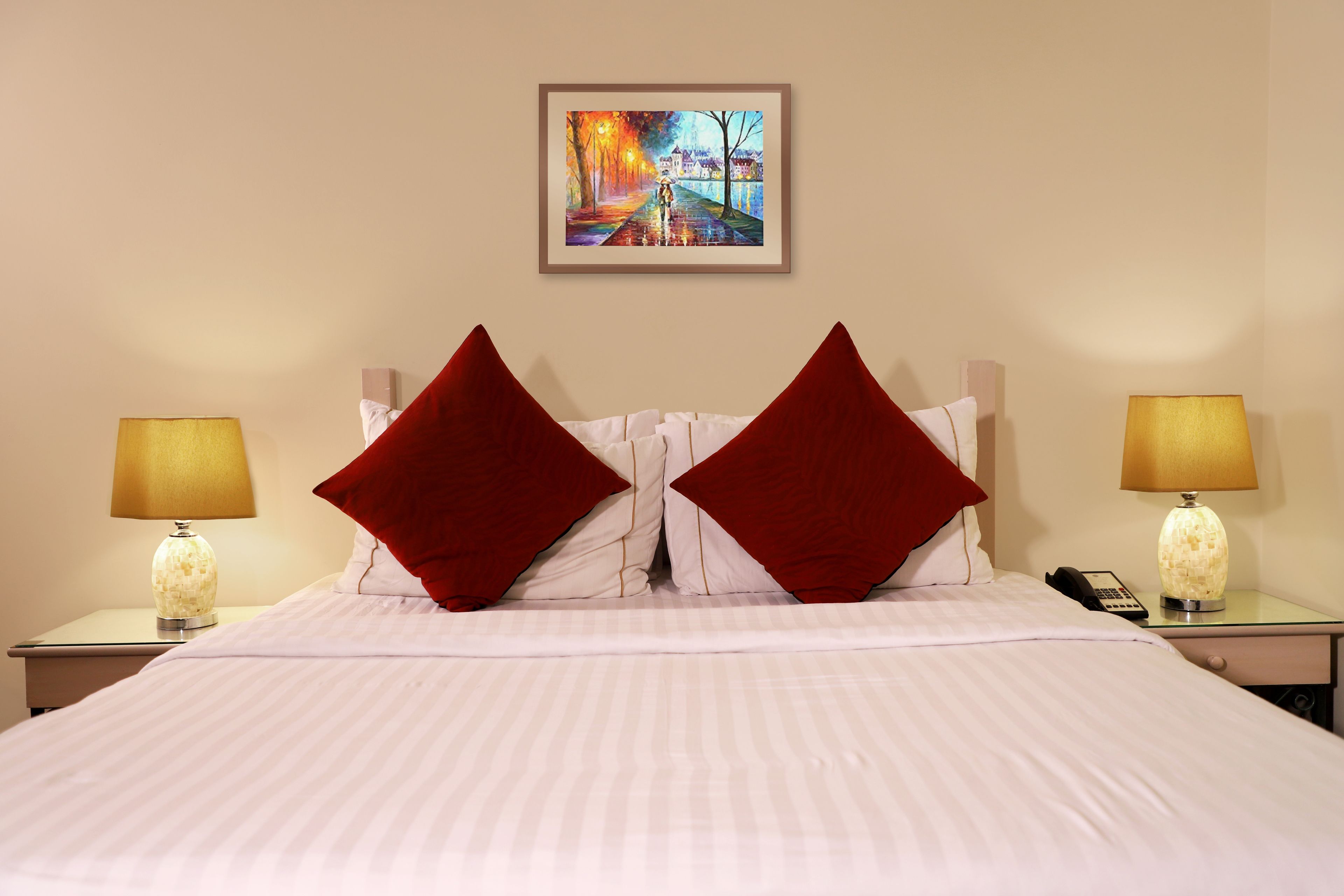 Een hotelkamer met een bed, twee nachtkastjes, twee lampen en een schilderij aan de muur.