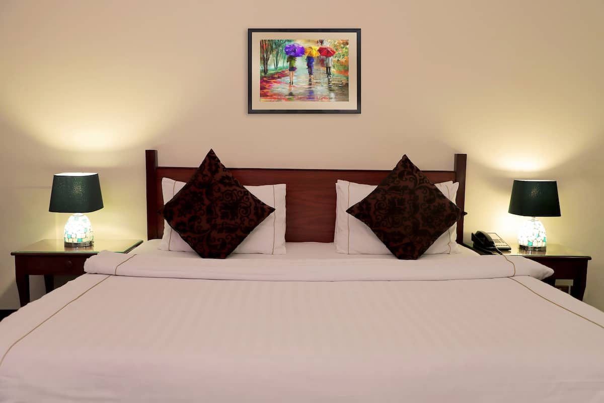A hotel room with a large bed, two nightstands with lamps, a painting on the wall, and patterned pillows.