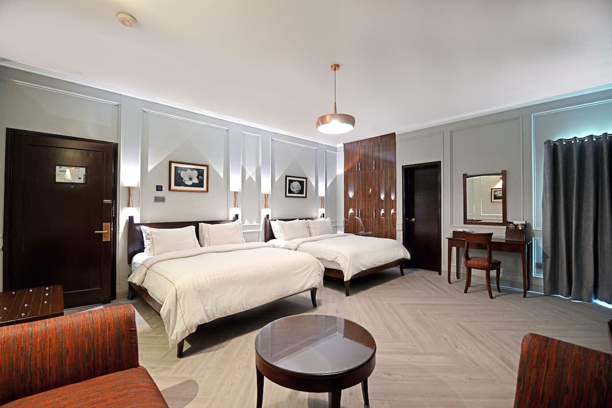 A hotel room with two beds, a desk, a chair, a round table, and a mirror.