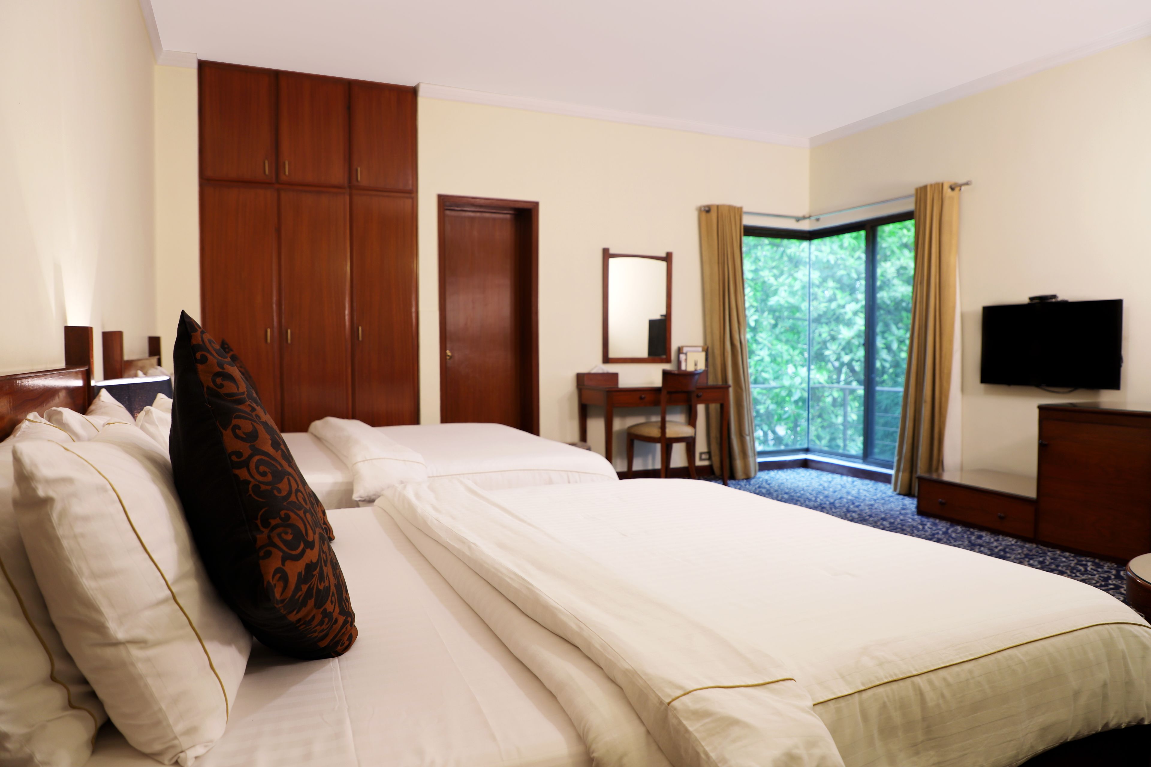 A hotel room with a large bed, a wardrobe, a desk with a chair, a television, and a window with curtains.