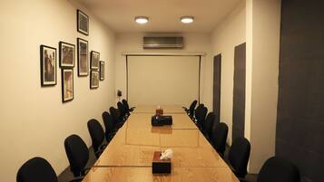 Un salón de conferencias con una larga mesa, sillas negras, cuadros en la pared y un equipo de aire acondicionado.