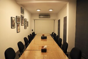 A conference room with a long table, black chairs, framed pictures on the wall, and an air conditioning unit.