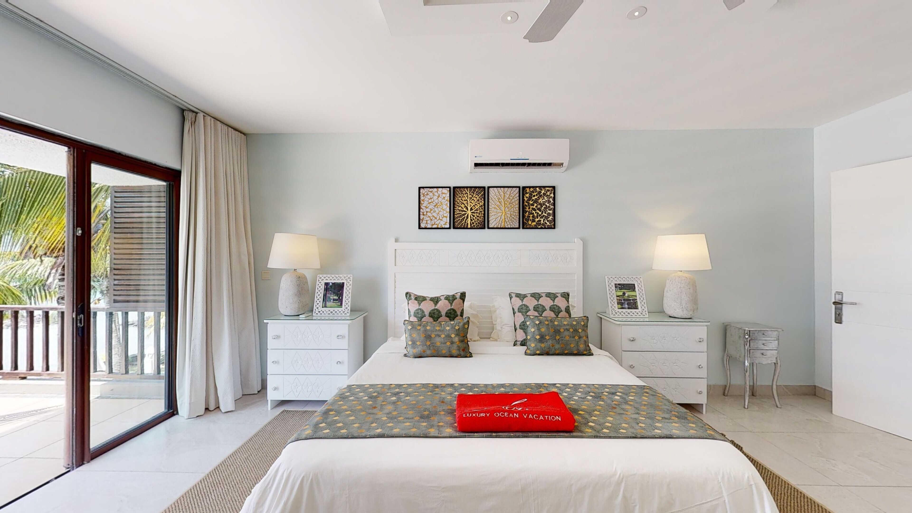 A bedroom with a large bed, two bedside tables, a ceiling fan, and an air conditioning unit.