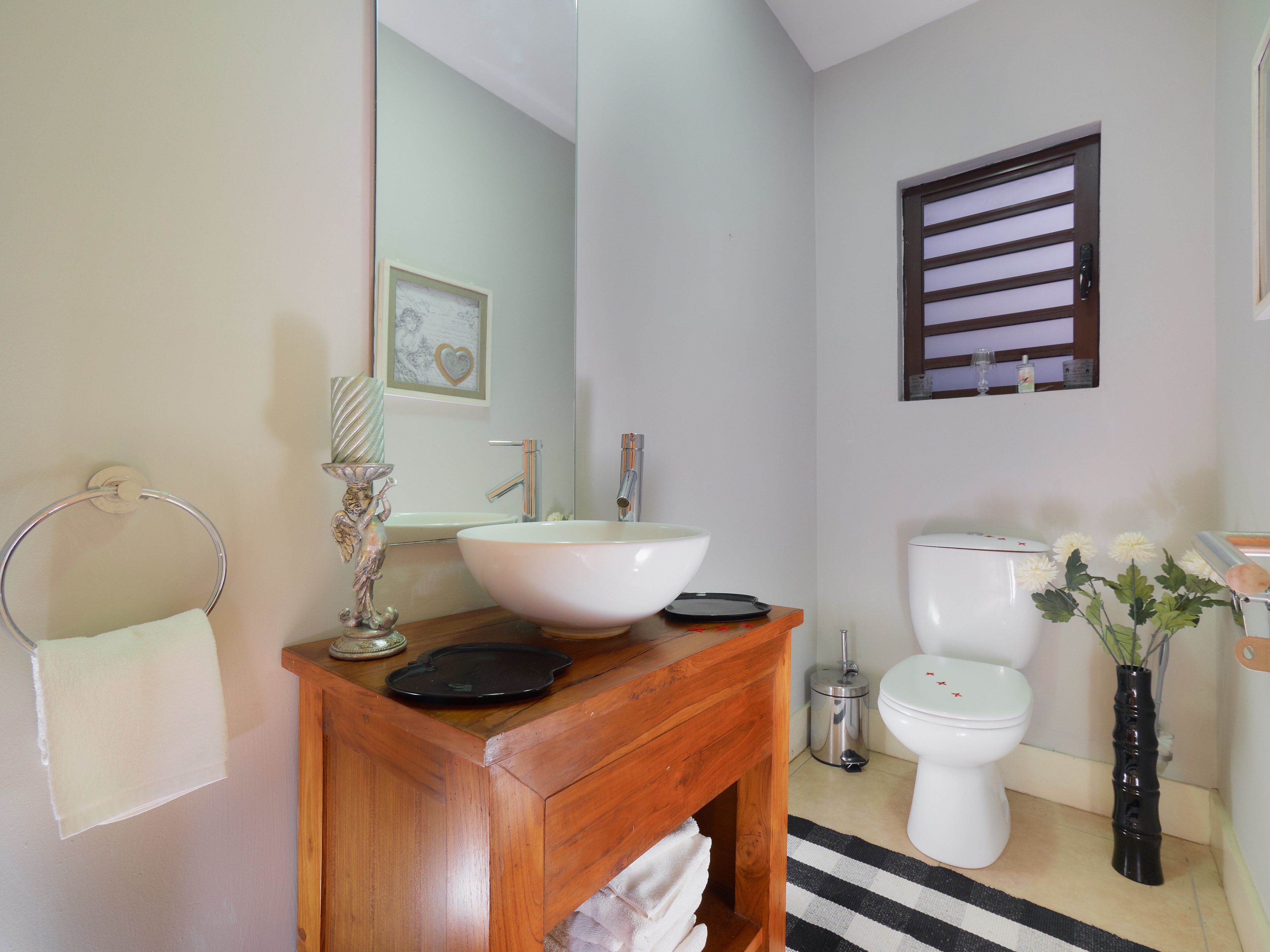 A bathroom with a wooden vanity, a white sink, a toilet, and a black and white striped rug.