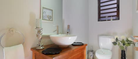 A bathroom with a wooden vanity, a white sink, a toilet, and a black and white striped rug.