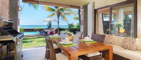 A dining area with a view of the ocean, a grill, and a sofa.