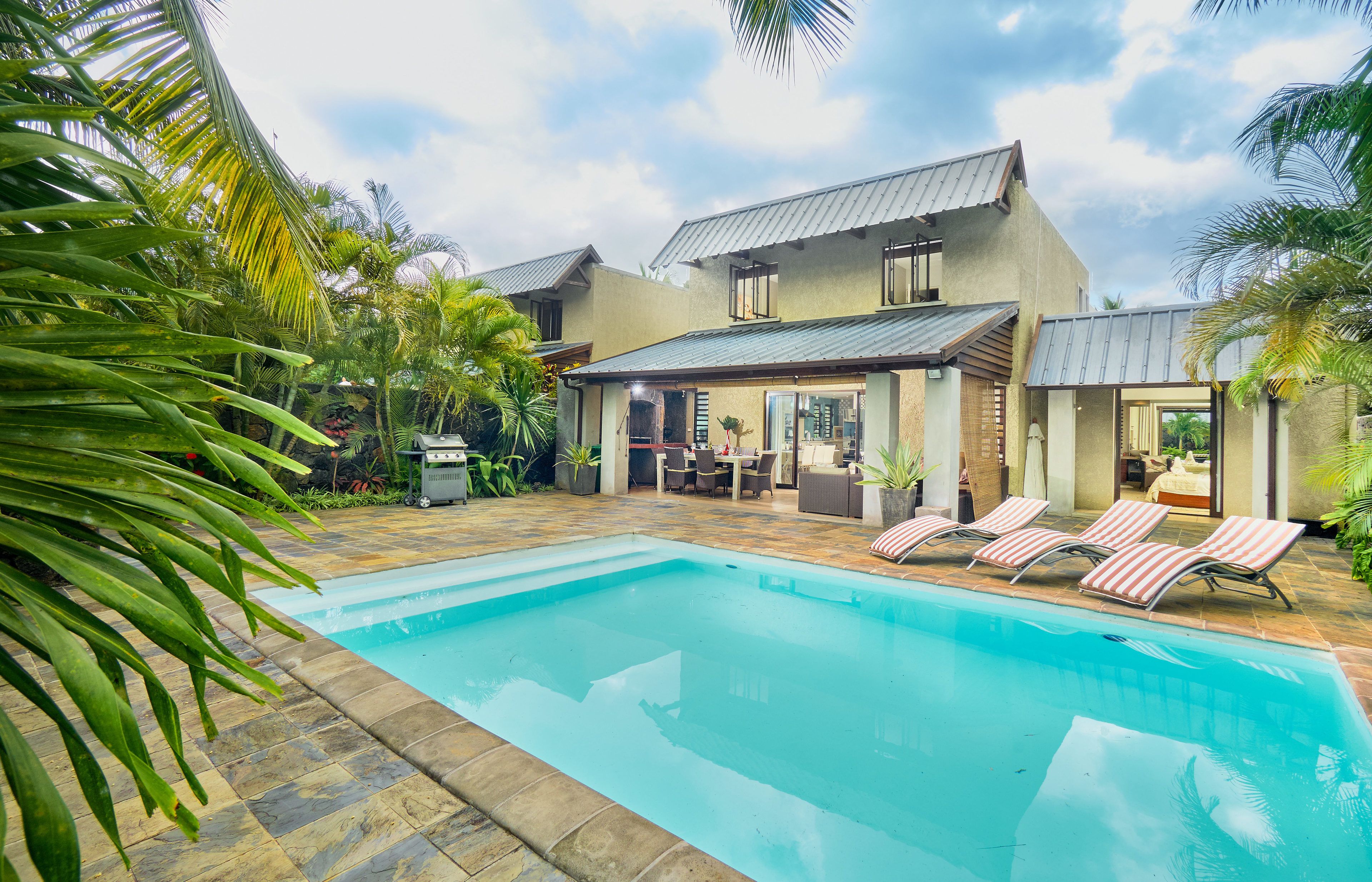 Ein modernes Haus mit Swimmingpool, Sitzgelegenheit im Freien und tropischen Pflanzen.