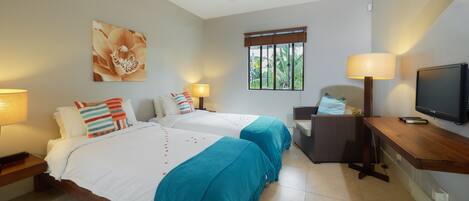 A hotel room with two beds, a television, a window with blinds, and a chair.