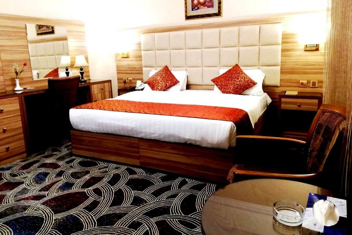 A hotel room with a large bed, two bedside tables, a chair, a desk, and a patterned carpet.