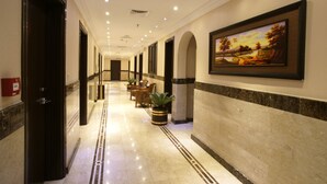 A hotel corridor with a marble floor, framed artwork on the wall, and potted plants along the walkway. - Roshan Al Azhar Hotel (Jeddah)