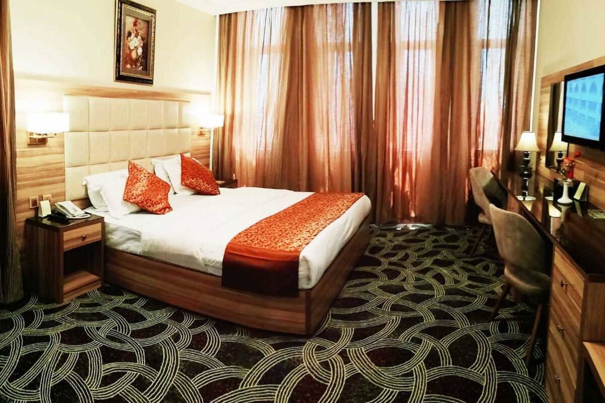 A hotel room with a bed, a desk, a chair, a television, and a patterned carpet.