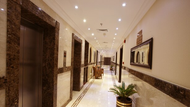 A long, well-lit hallway with marble flooring, a potted plant, and a wooden chair. - Roshan Al Azhar Hotel (Jeddah)